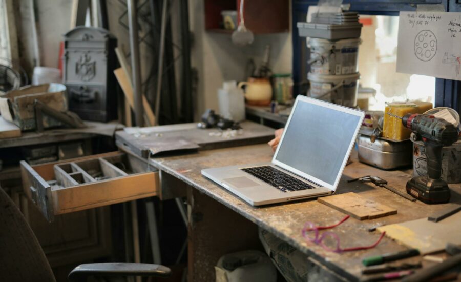 From above of modern laptop laying at table among different tools and equipment in workshop